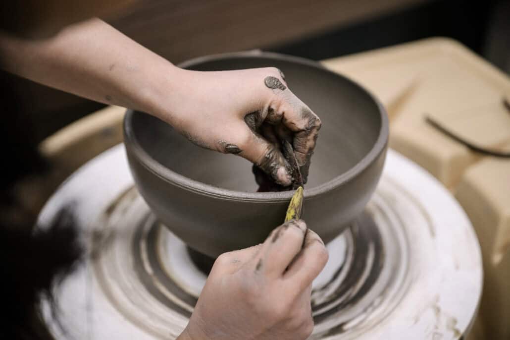 Hands trim the rim of a wide clay bowl as the potter's wheel turns in a pottery studio in Japan
