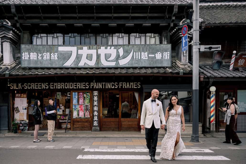 The newlyweds cross Kawagoe's kurazukuri street hand in hand in front of an old merchant shop, visitors all around them.