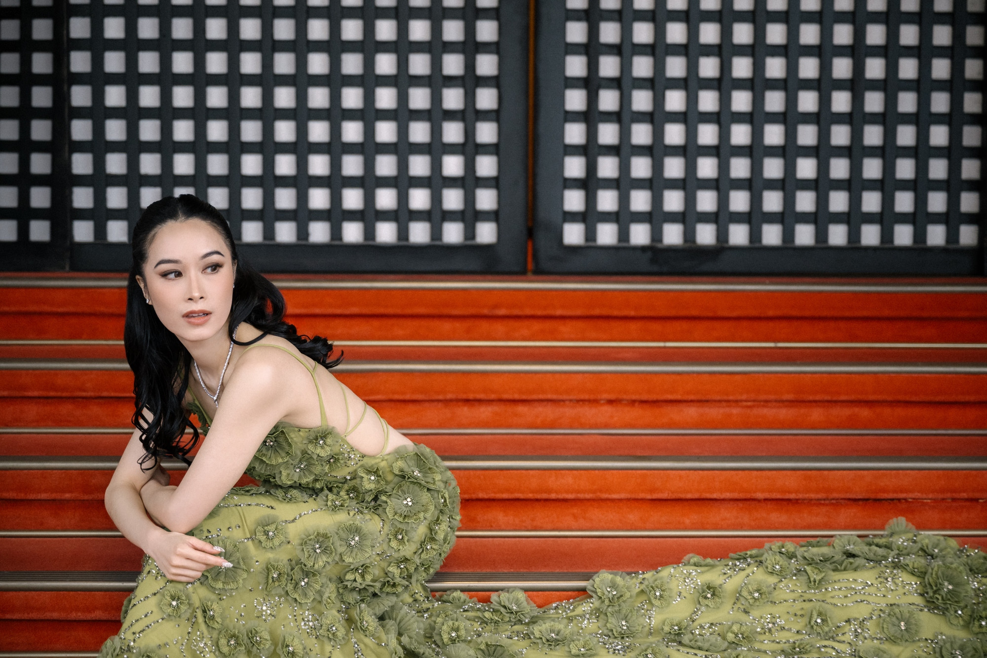 A bride in a green couture gown sits on the red-carpeted steps of Meiji Kinenkan in Tokyo, black lattice doors behind her, on a welcome dinner night.