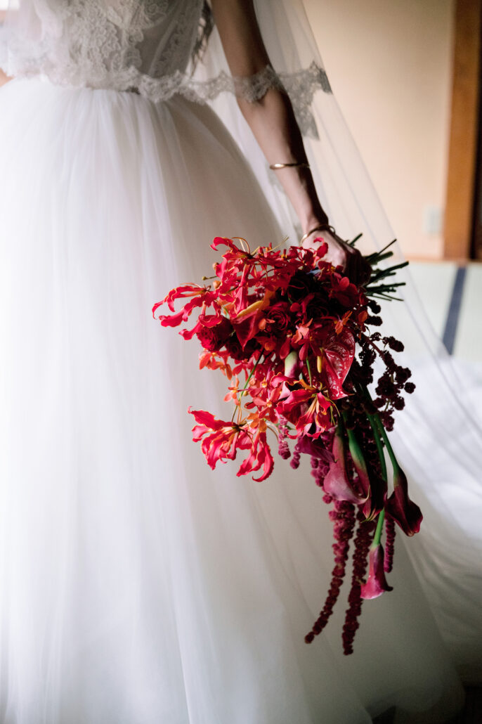 A cascading bouquet of deep red flowers and trailing amaranthus against the bride's white tulle, made by a florist in Japan for a wedding at Jinya.