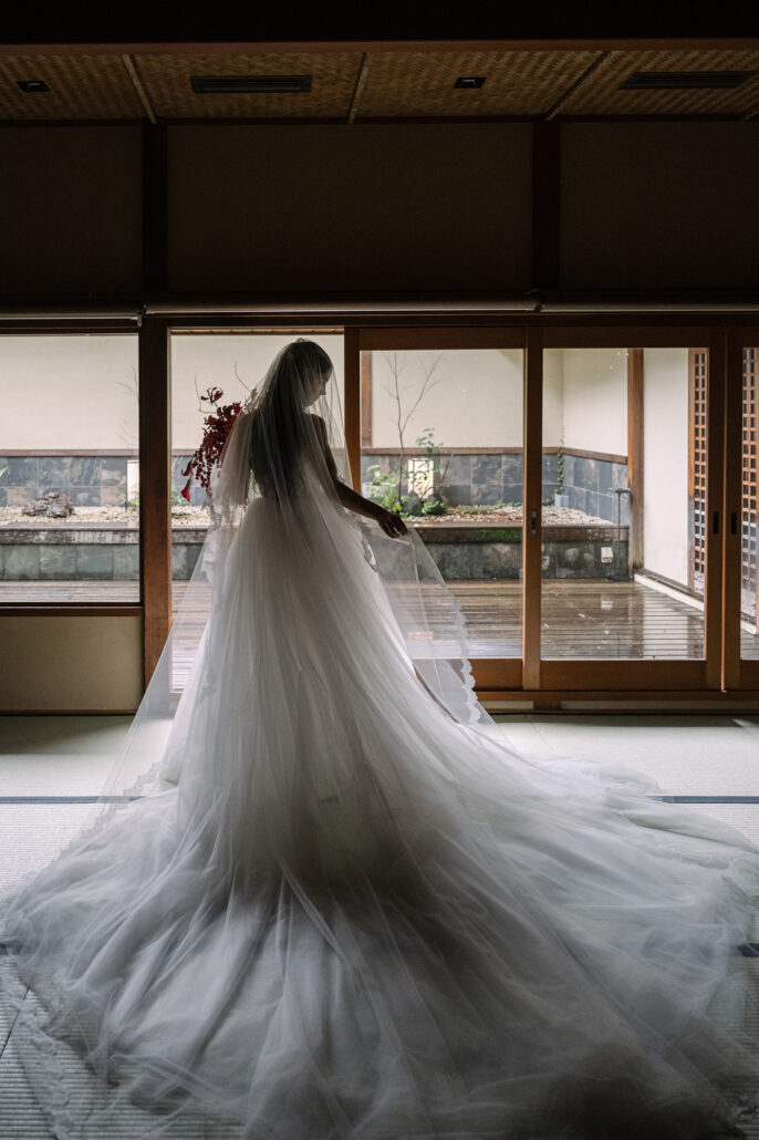 The bride stands with her back to the camera, her train fanned out, looking out to the Japanese garden at Jinya.