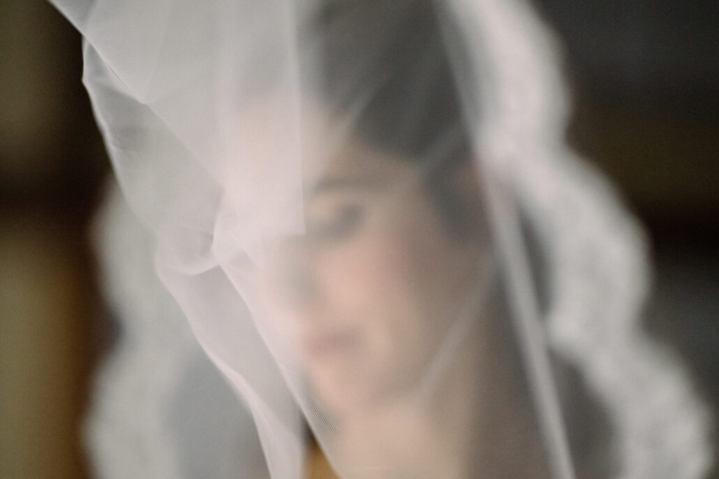 The lace edge of the veil falls soft across the frame as the bride looks down.