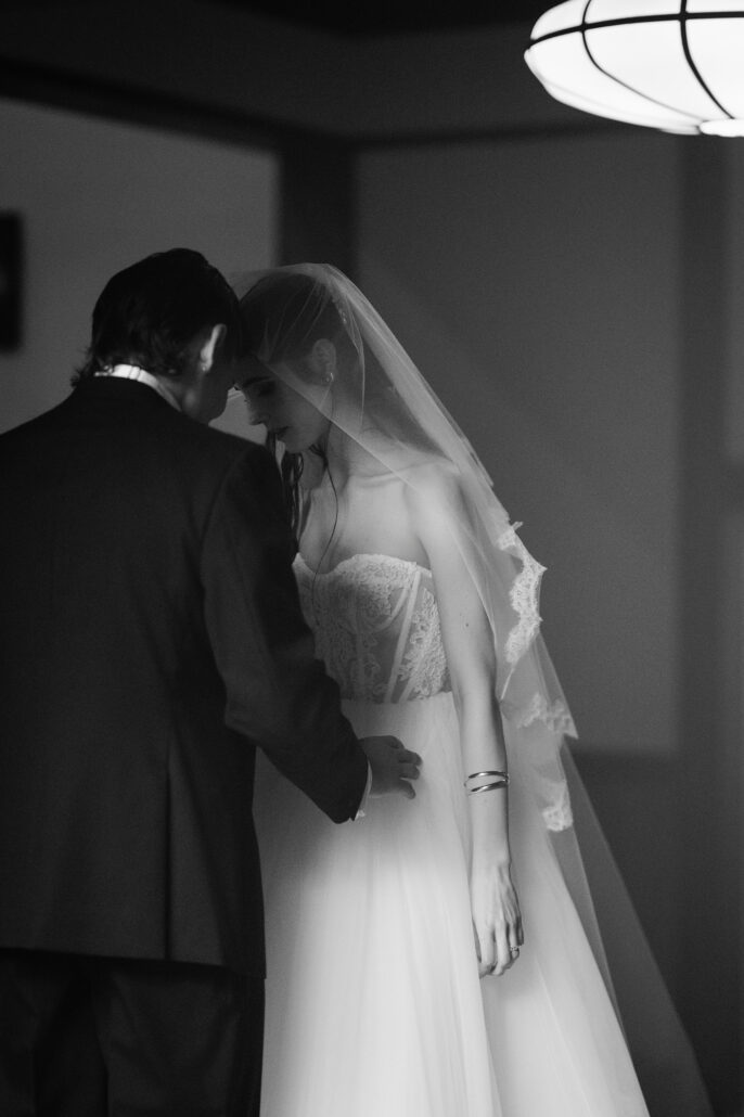 In black and white, the bride and groom lean in close, foreheads together.