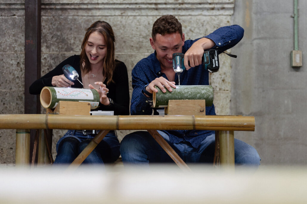 The couple sit at a wooden bench drilling patterns into bamboo lanterns at a craft workshop in Japan.