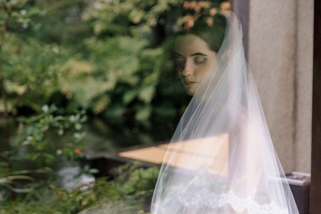 The bride's reflection in the glass, layered over the green of the garden outside.