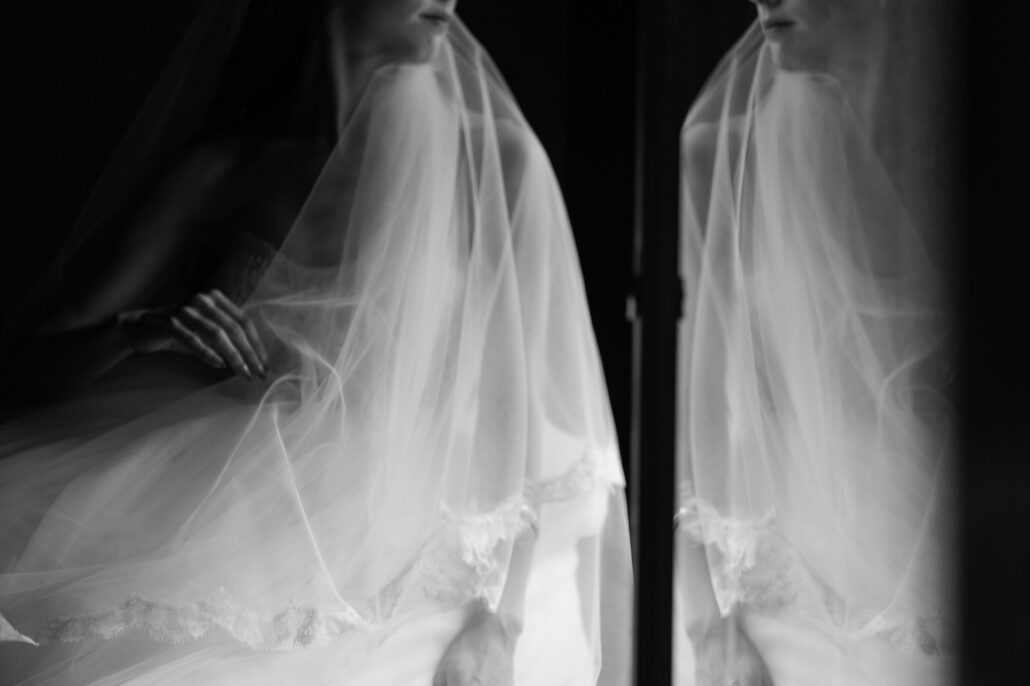 In black and white, the bride's veil and its reflection side by side in the window glass.