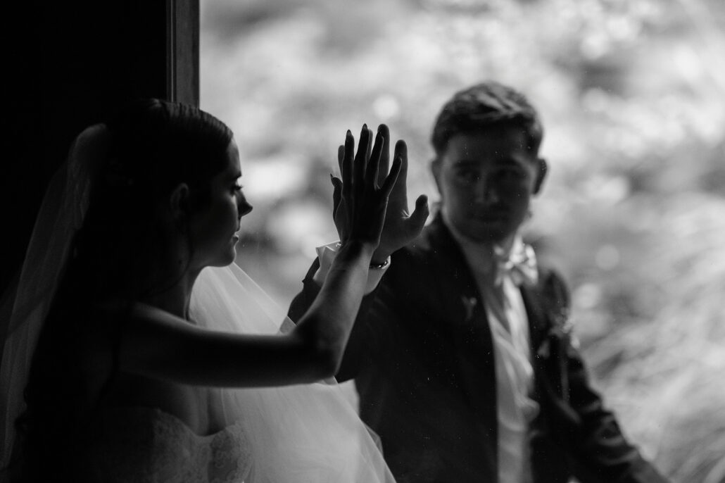 Black and white photograph of a bride and groom pressing their hands together through a pane of glass at a ryokan wedding in Japan