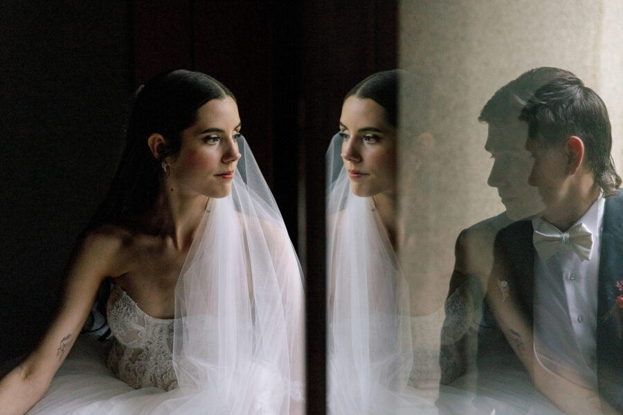 The bride by a window at Jinya, the groom reflected in the glass beside her, a portrait on their wedding day.