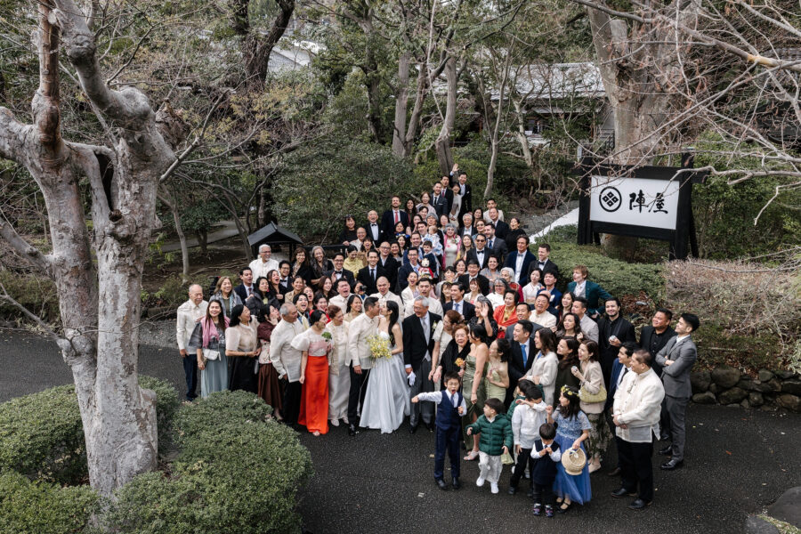 All the wedding guests gather around the couple beneath the Jinya sign in the garden, seen from above.