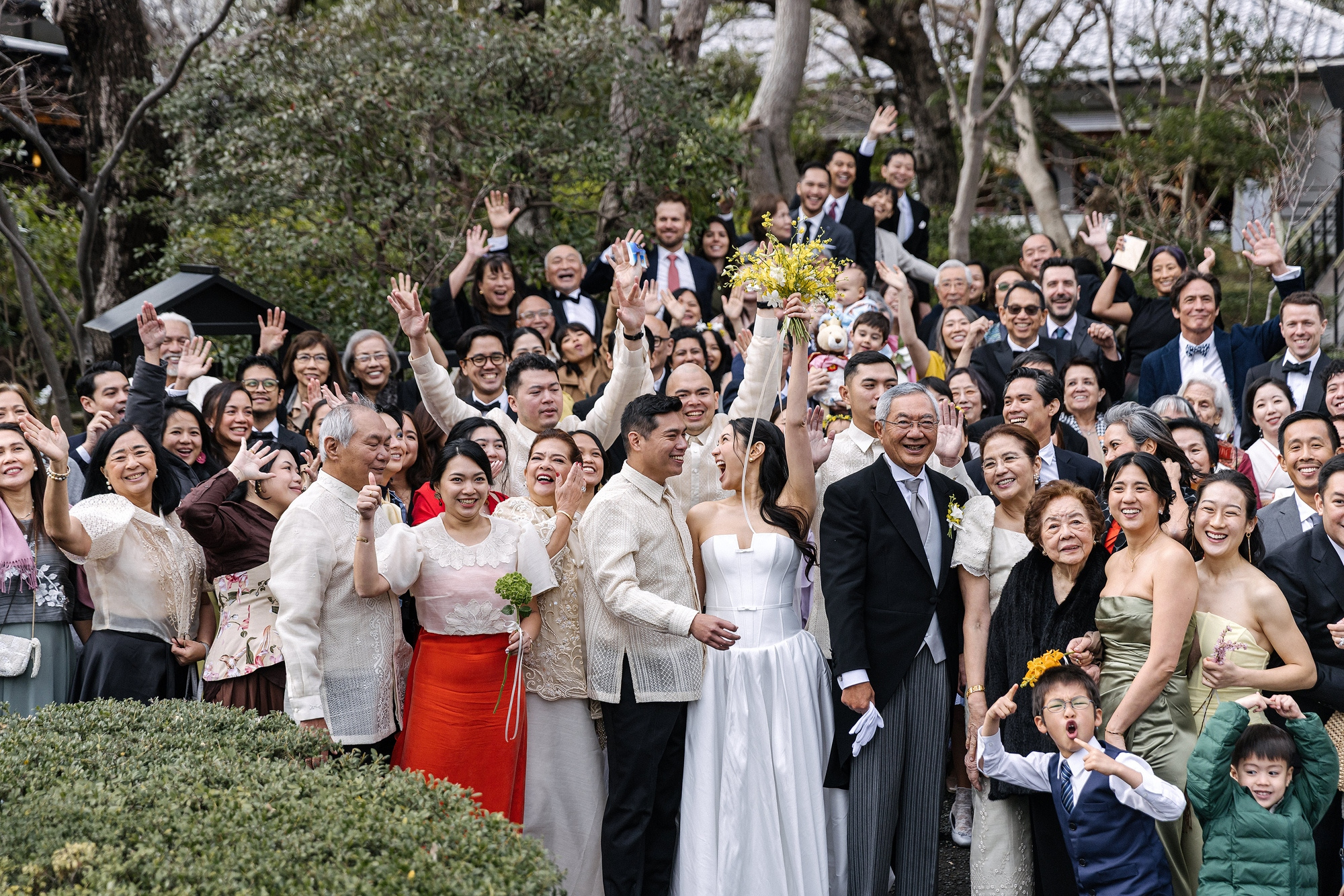 Guests wave and cheer around the couple for the group photograph after an onsen wedding in Kanagawa, everyone who made the trip to attend a wedding in Japan.