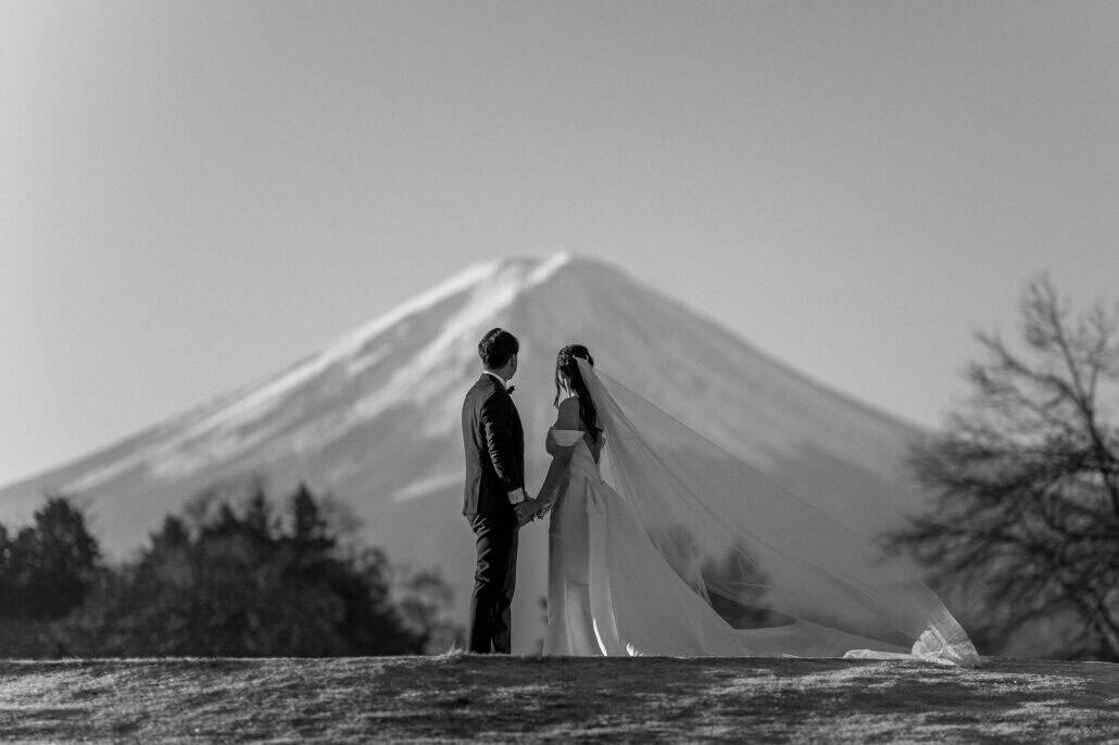 A black and white frame of the couple holding hands before a clear Mt Fuji the morning after their wedding.