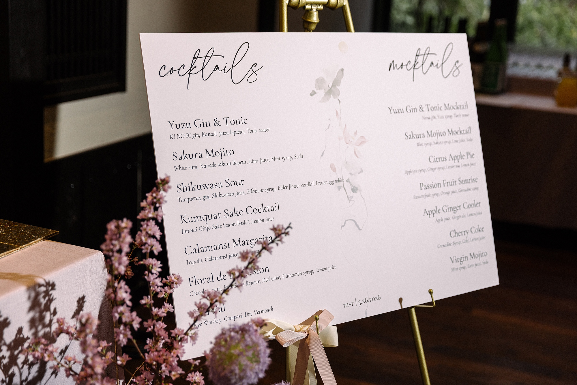 A wedding reception drinks board lists cocktails beside a full mocktail menu, with pink blossom in front, at a ryokan wedding in Japan.