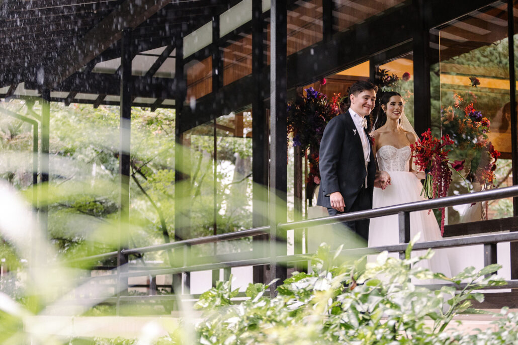 The bride and groom on the veranda over the garden, seen through soft green leaves.