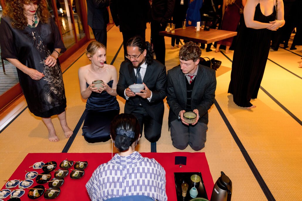 Wedding guests kneel on tatami holding bowls of matcha made in front of them during cocktail hour at a ryokan in Japan