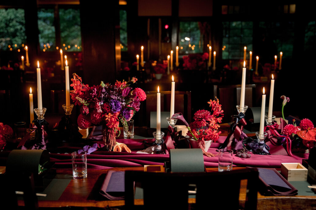 A candlelit gothic wedding reception at Jinya, with red and purple flowers, ivory tapers on crystal candlesticks and masu cups at each place.