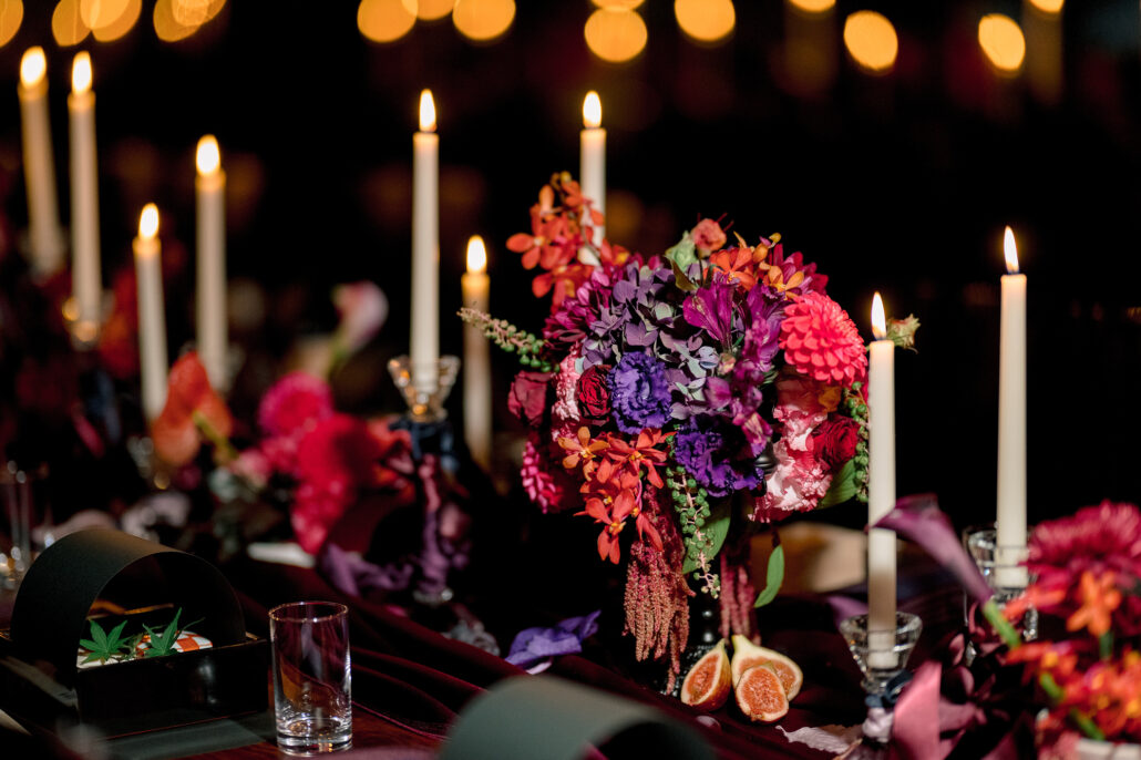 A gothic wedding centrepiece of dahlias, orchids and purple lisianthus, amaranth trailing, with figs cut open and ivory tapers at Jinya.