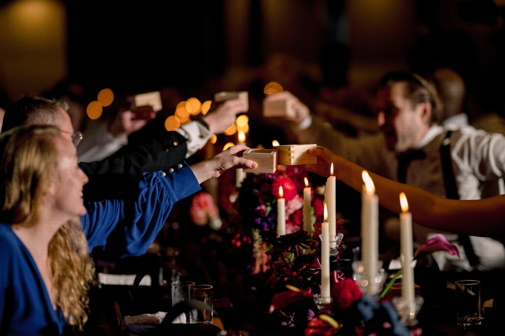 Guests toast with masu cups across the candlelit reception table.