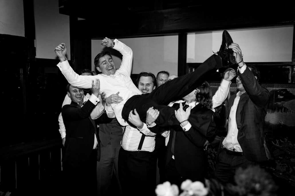 In black and white, the groom flies above his friends' hands.