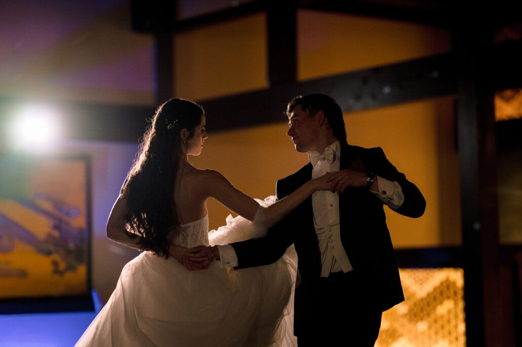 The bride and groom begin their first dance in the warm light of the room, gold screens behind.