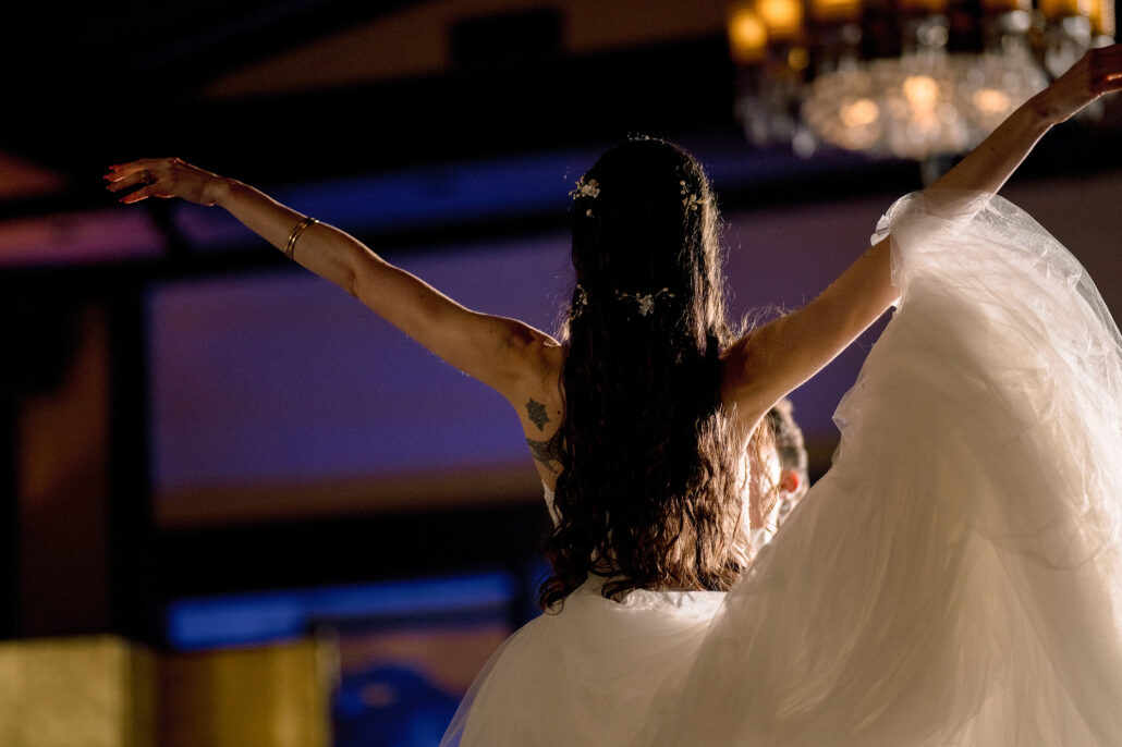 The bride throws her arms wide during the first dance under the chandelier.