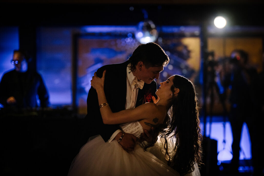 The groom dips the bride under blue light during their first dance, the DJ behind them.