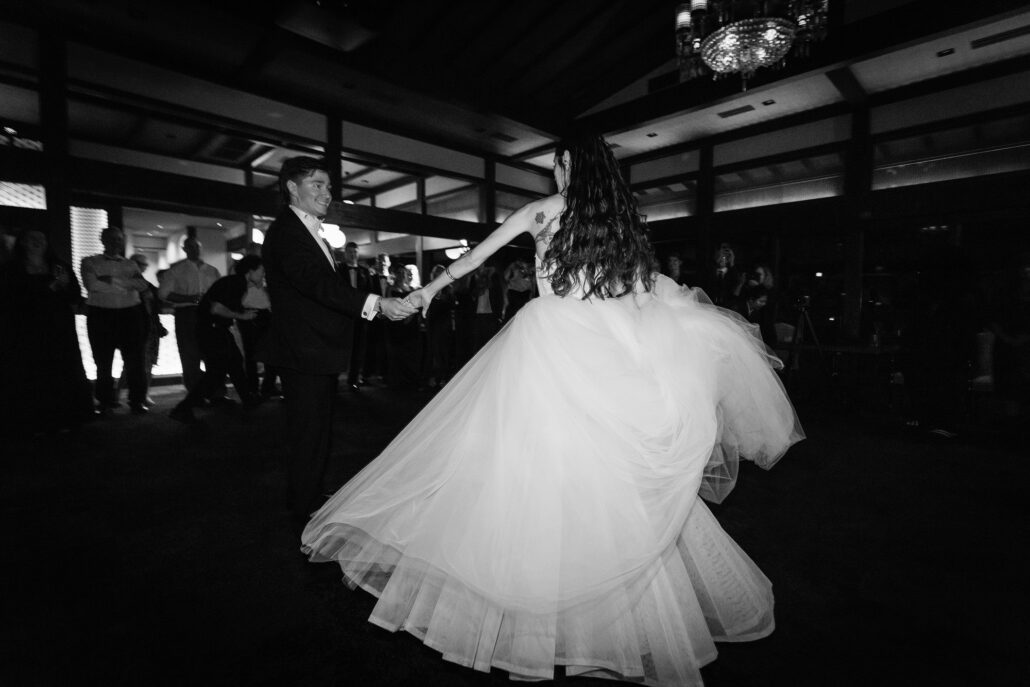 In black and white, the bride's gown swirls out as they turn in their first dance.