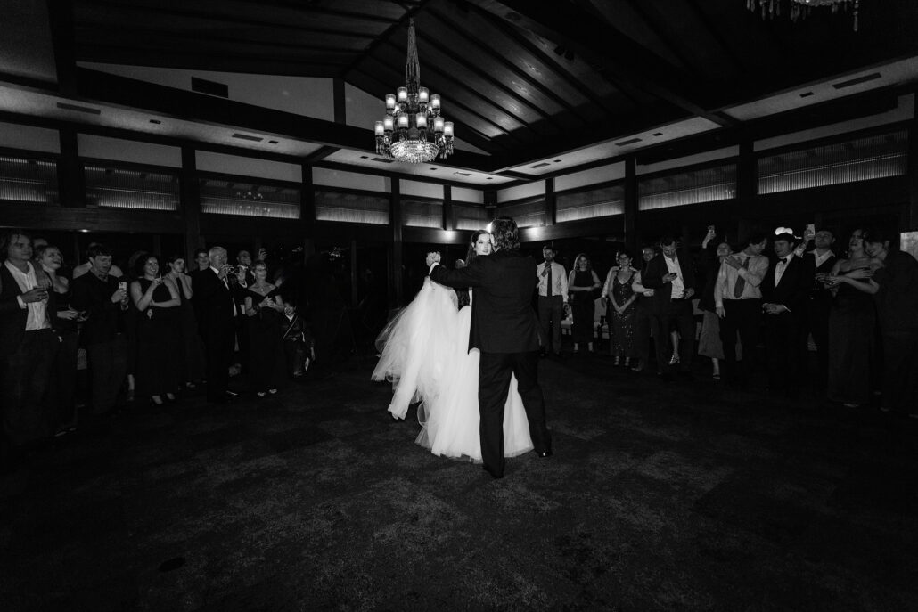 In black and white, the couple alone on the floor with guests all around.