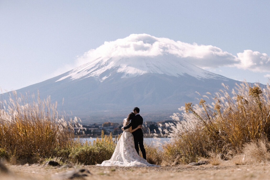 Seen from behind, the couple look out at Mt Fuji and its cap cloud between banks of silver grass.