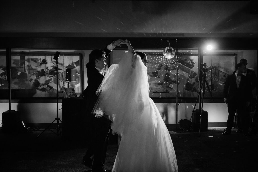 In black and white, the bride spins as the groom holds her hand above her.