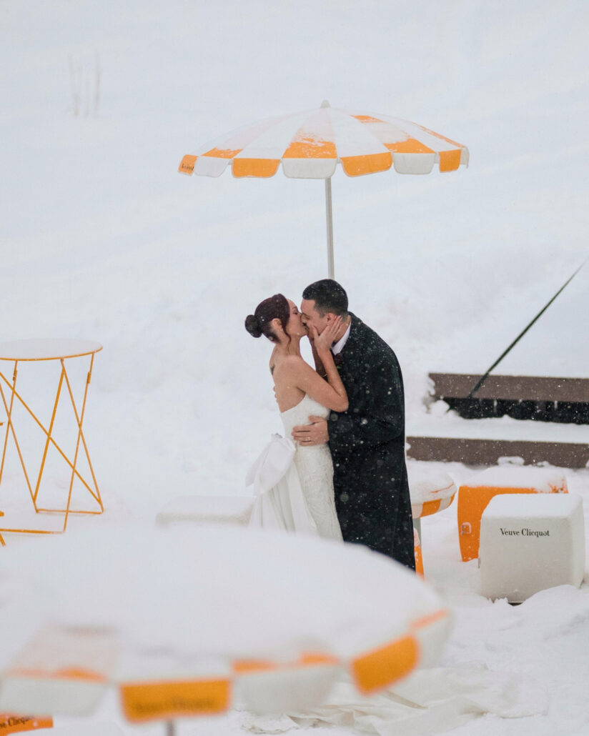 The couple kiss beside snow capped orange and white umbrellas at the apres ski cocktail hour on the slope, a quiet pause in a Hakuba snowstorm.