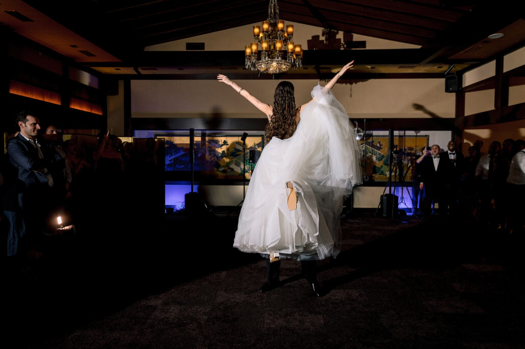 The groom lifts the bride high at the end of their first dance, under the chandelier.