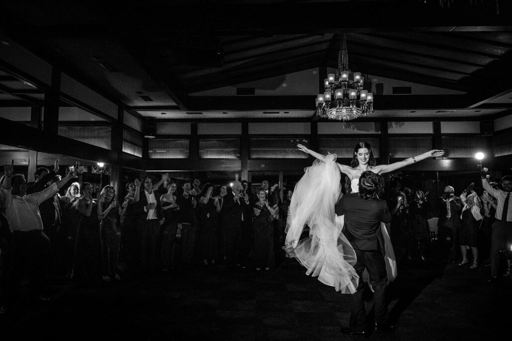In black and white, the bride lifted high above the floor as guests watch.