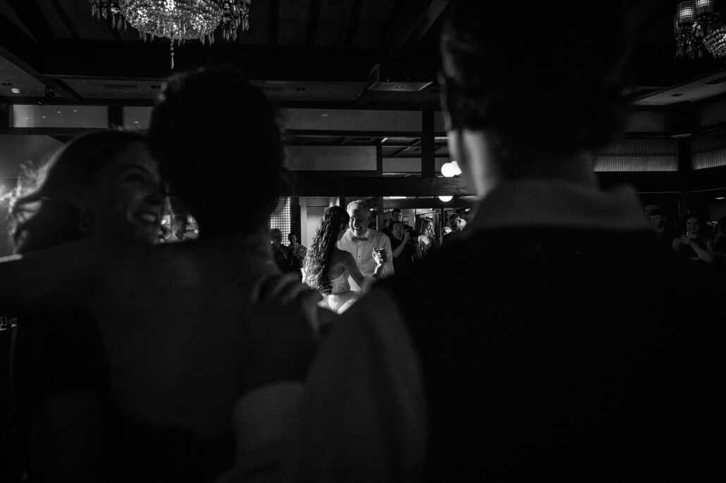 In black and white, guests watch the parent dances from the edge of the floor.