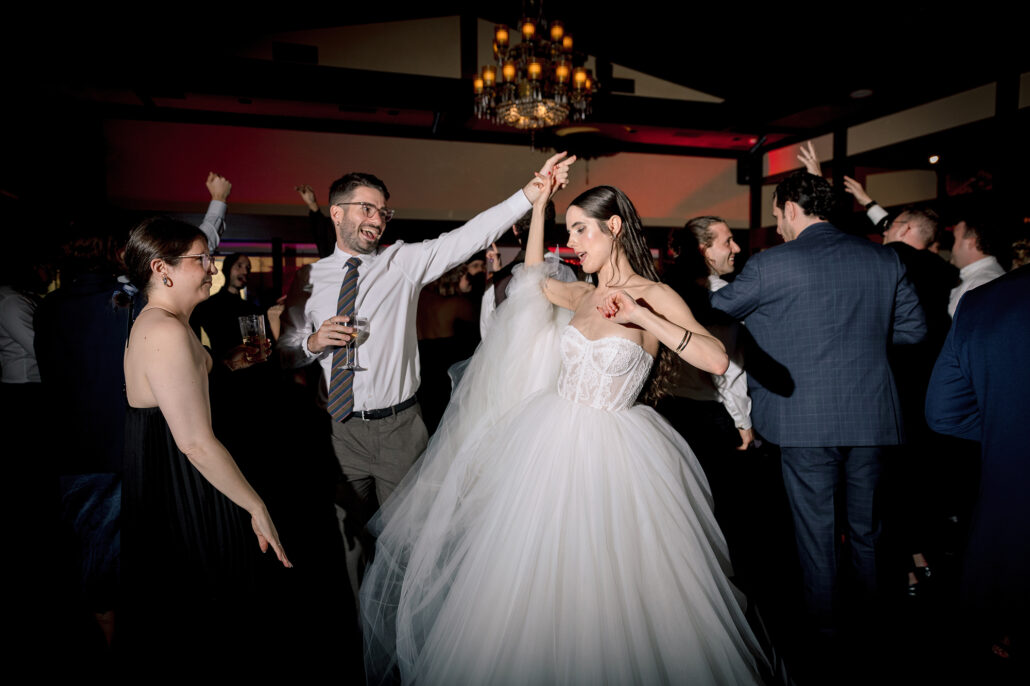 The bride dances with a guest under the chandelier as the dance floor fills.