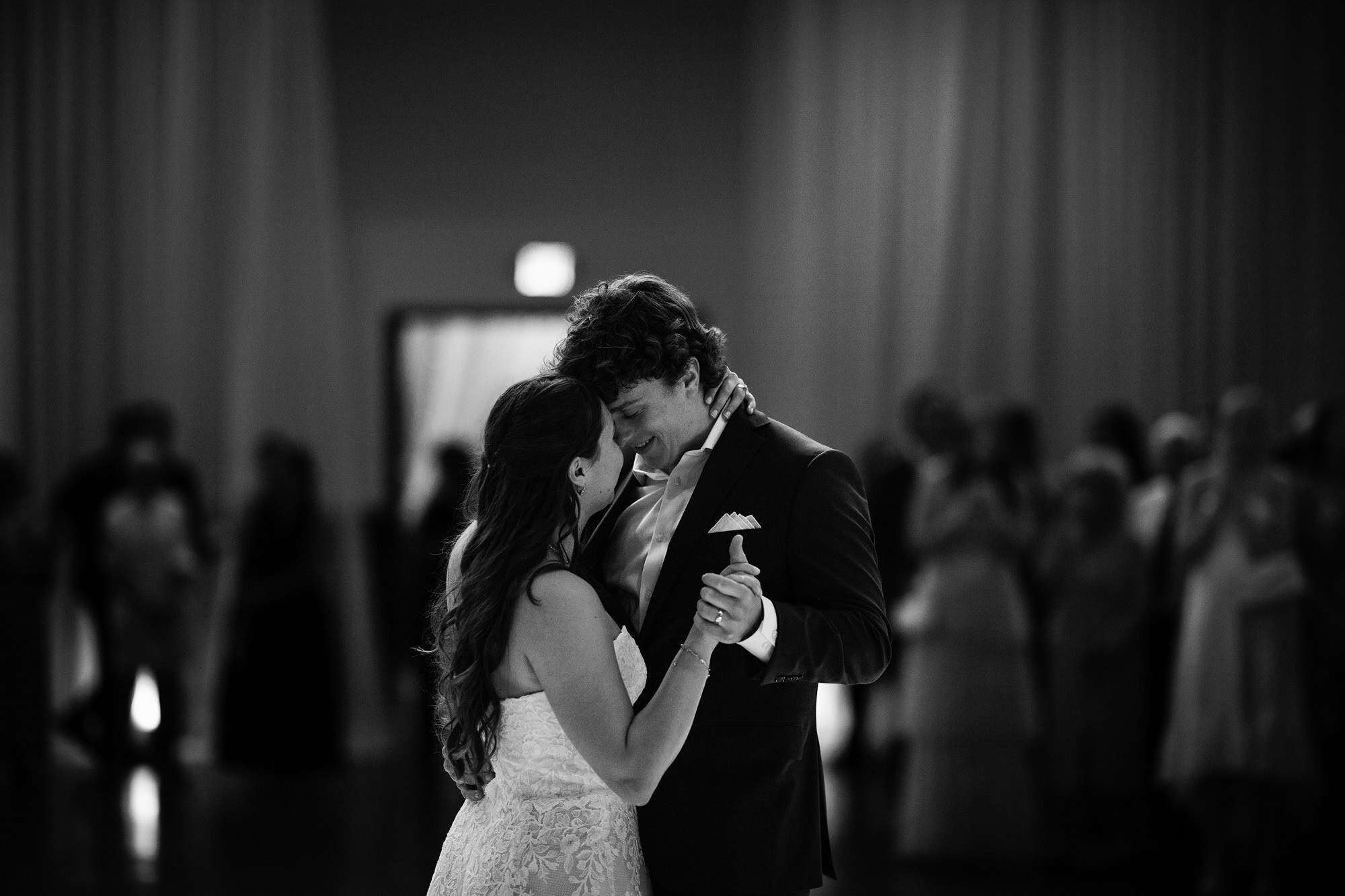 In black and white, the couple hold each other close for their first dance of the second night, guests watching in the dark.