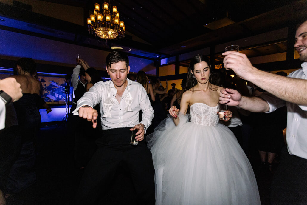 The groom dances with a drink in hand as the bride dances beside him.