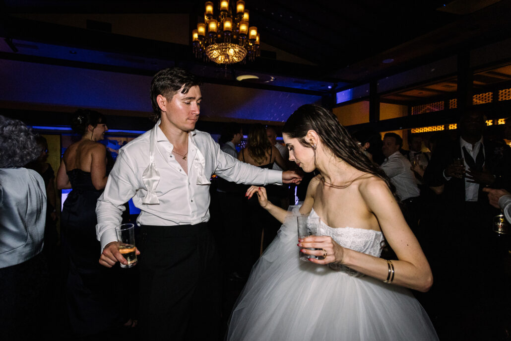 The couple dance with their glasses, guests close around them.