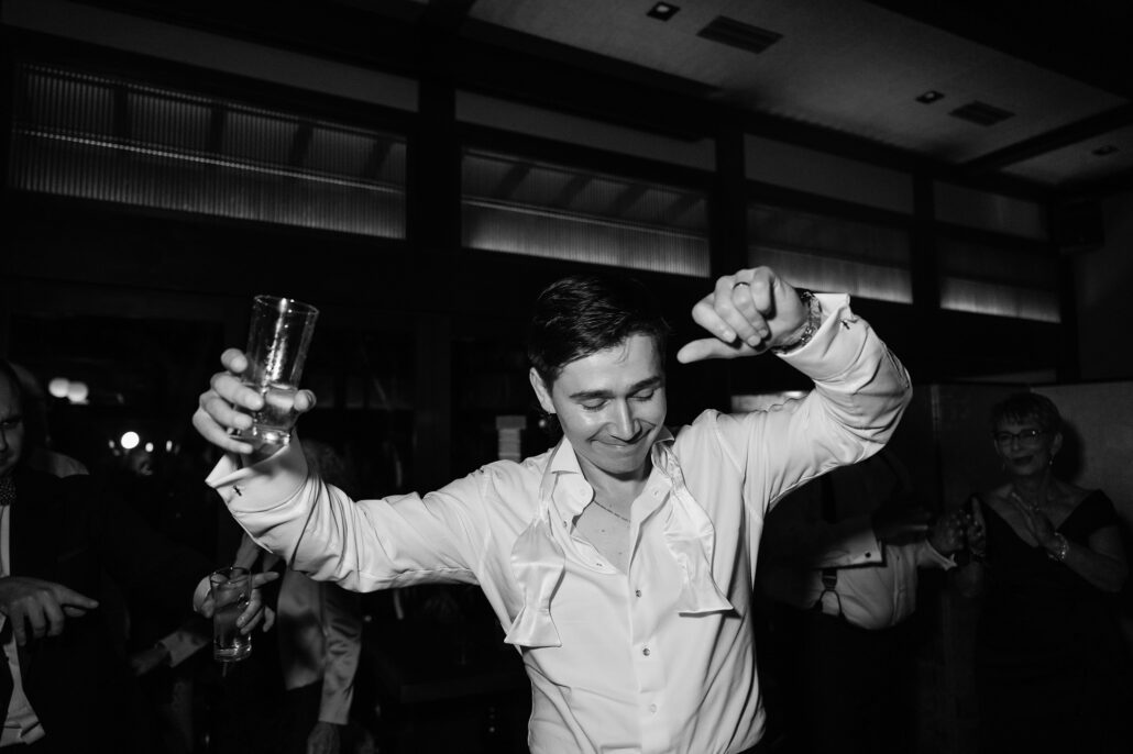 In black and white, the groom dances with his glass held high.