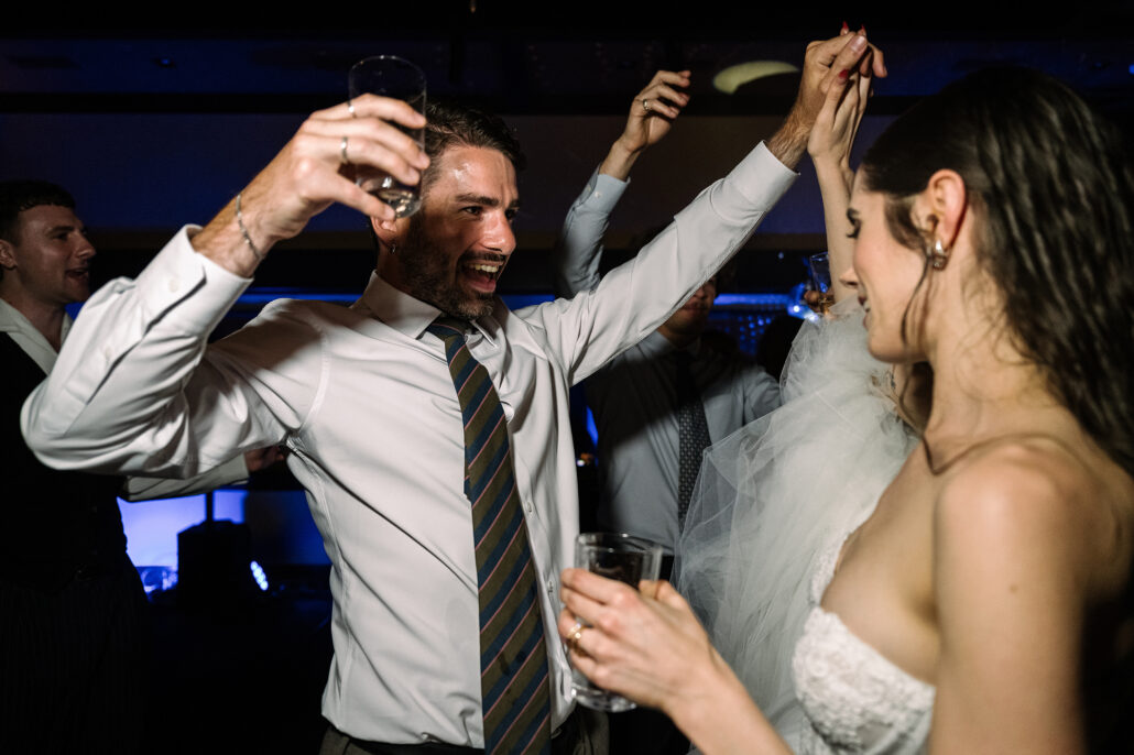 A guest in a tie dances with his glass raised beside the bride.
