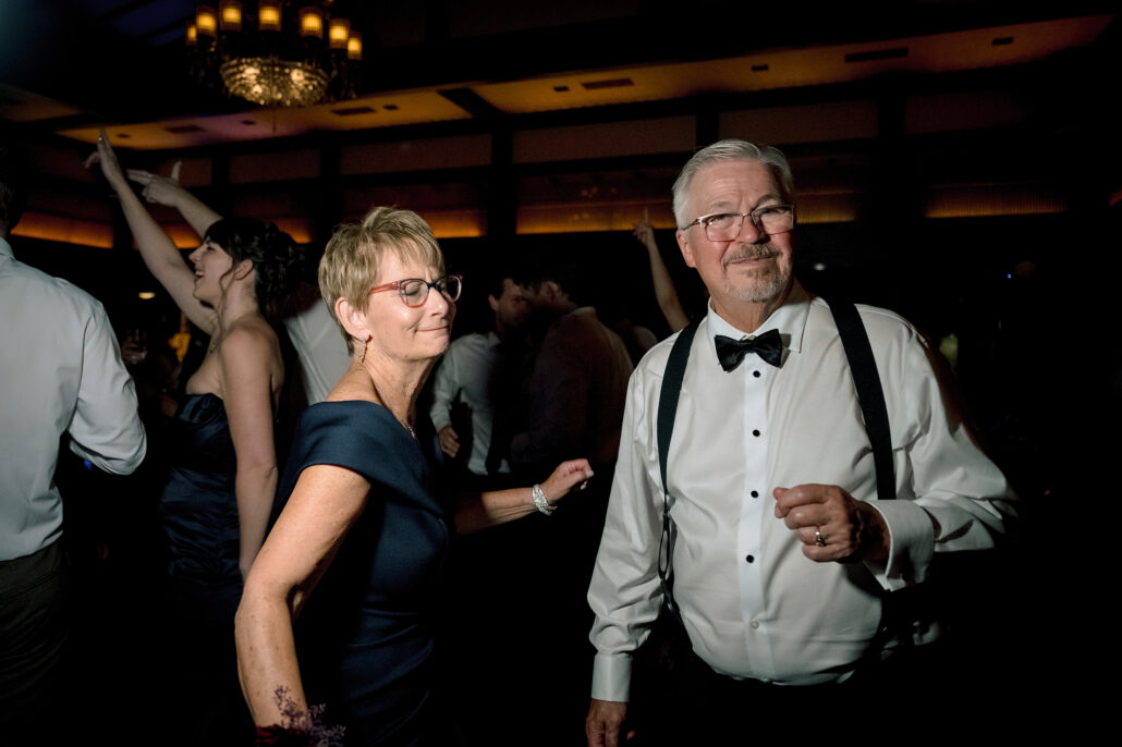 Two guests dance on the crowded floor, a woman in navy and a man in a bow tie and braces.