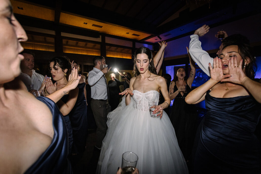 The bridesmaids in navy cheer around the bride on the dance floor.
