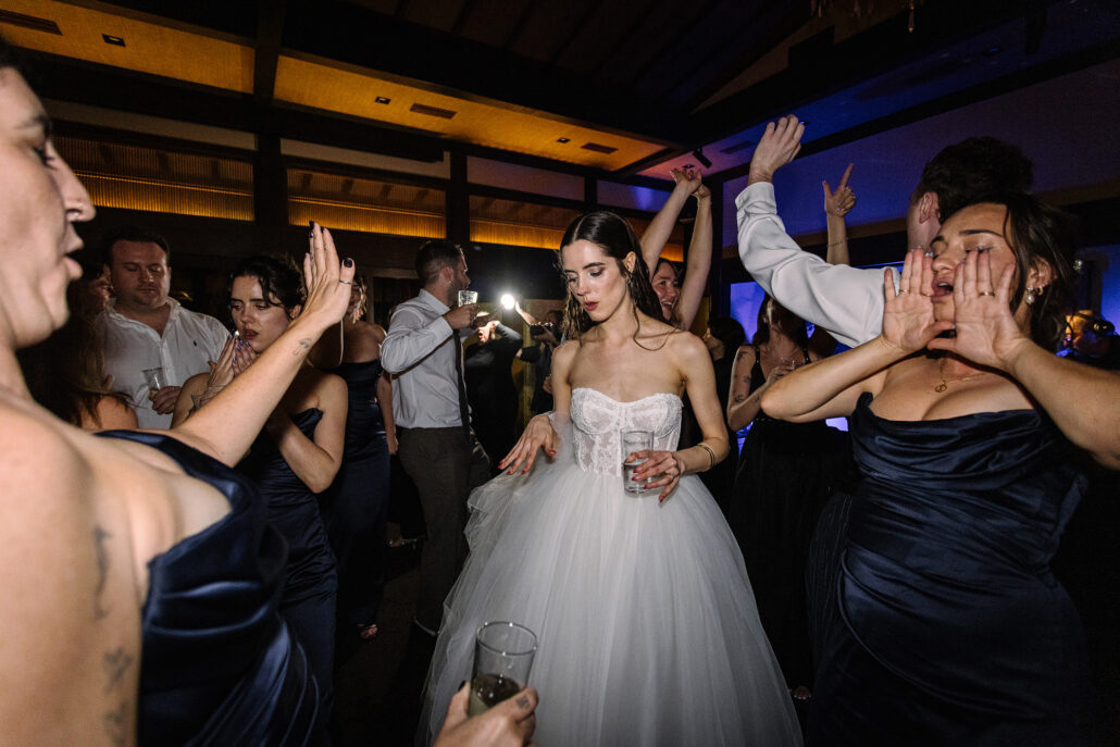 The bride dances with her bridesmaids, one of them shouting with her hands to her mouth.