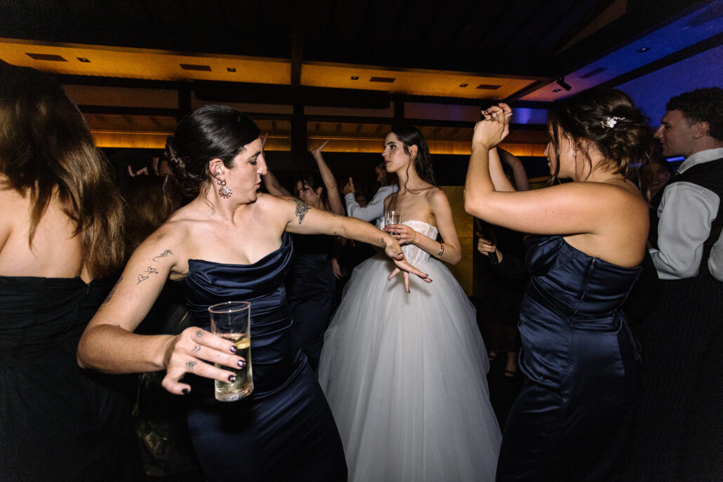 The bridesmaids dance around the bride as the room fills.