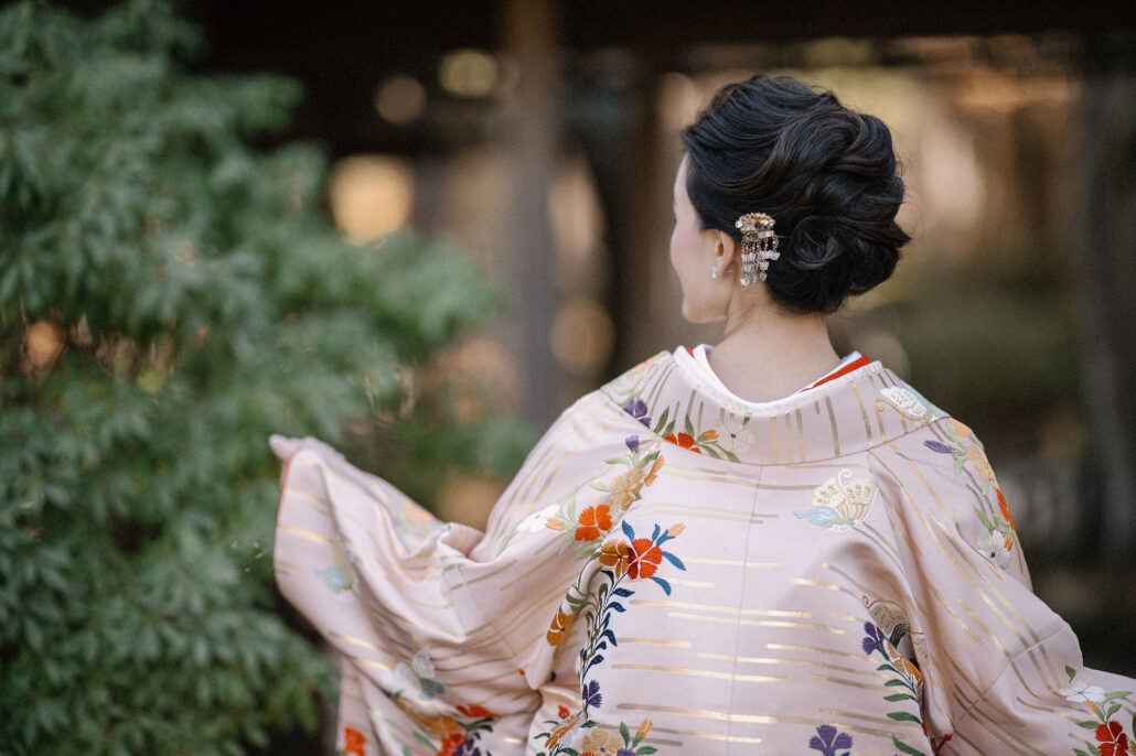 Seen from behind, the bride turns and her uchikake sleeve swings out in a blur of pink, gold and flowers.