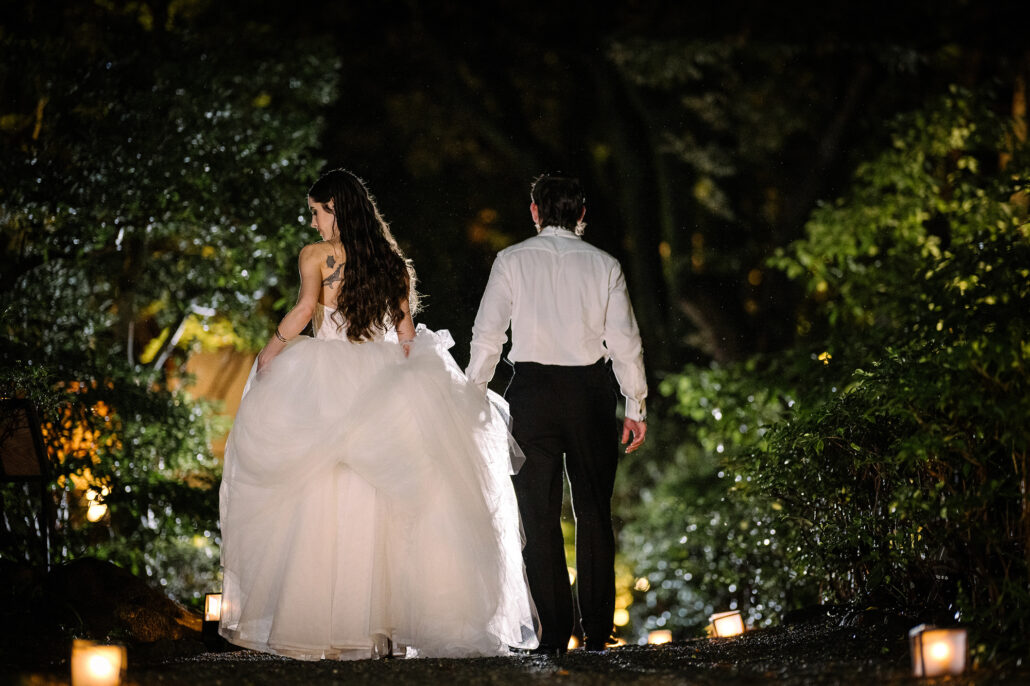 The bride and groom walk away along a garden path lined with small lanterns on the night of their wedding in Japan