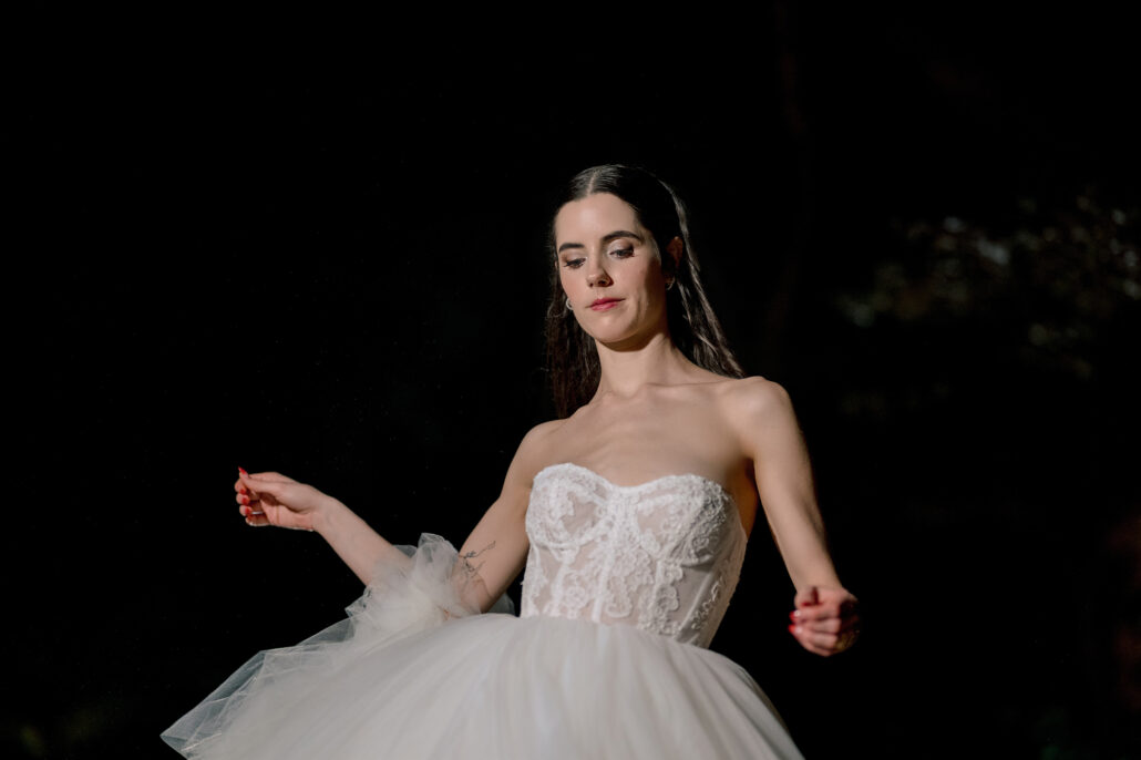 The bride twirls her skirt alone in the dark of the garden.
