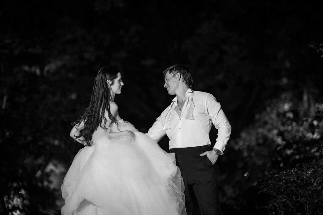 In black and white, the bride and groom laughing together in the dark.
