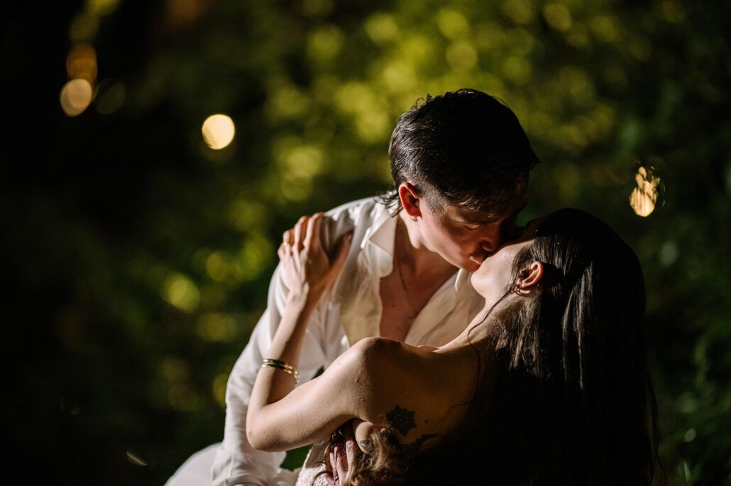 The couple kiss in the dark, warm lights blurred behind them.