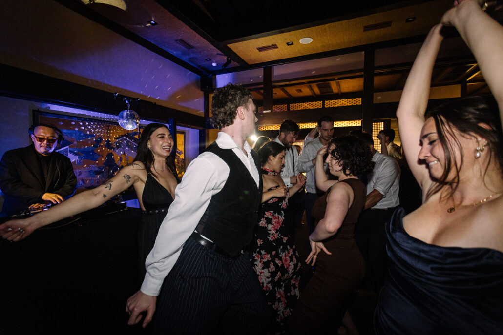 A guest in a waistcoat dances among the bridesmaids late at night.