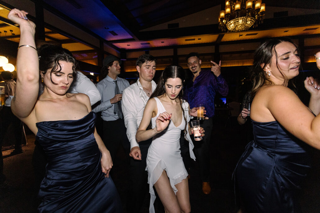 The bride dances with her bridesmaids in navy late in the night.